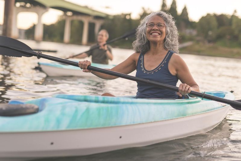 A senior woman smiles while kayaking with her husband