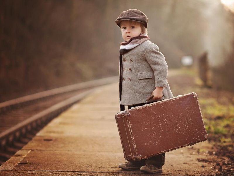 Adorable boy on railway station, waiting for train with suitcase