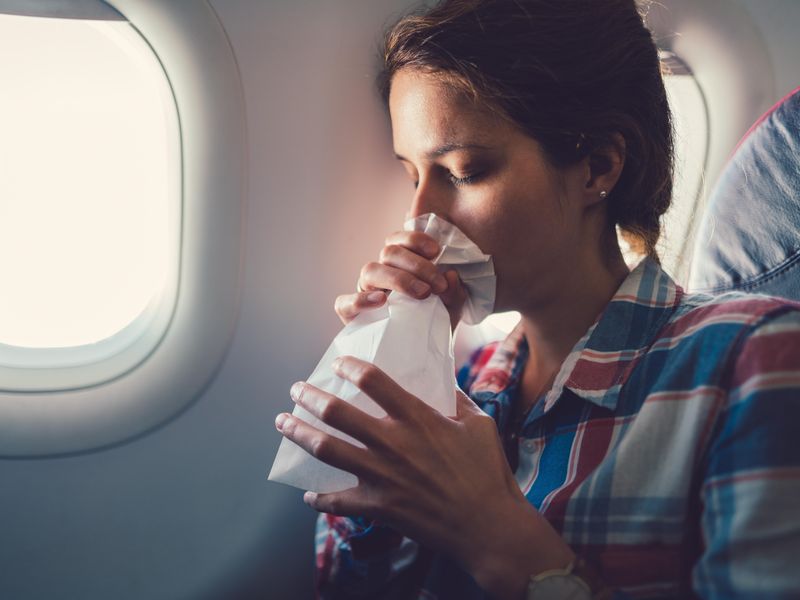 Anxious woman on airplane breathing in vomit bag