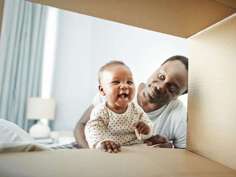 Baby girl and her father playing with a cardboard box at home