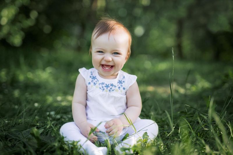 Baby girl sitting on grass in the park and laughing