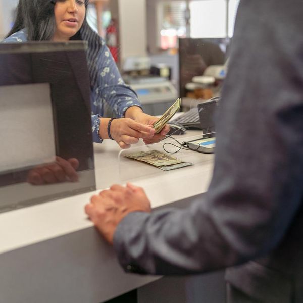 Cropped shot of a female bank teller counting US Currency for a male customer at the counter in a bank. Selective focus on the bank teller's hands holding the money.