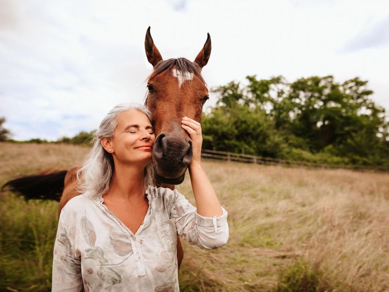 Beautiful mature woman enjoying with closed eyes her brown arabian mare in the free nature