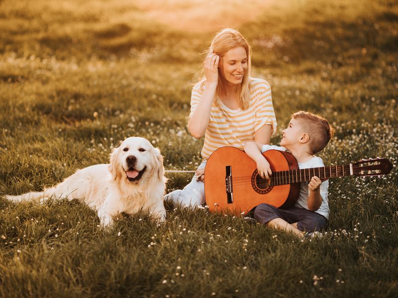 Boy playing guitar for his happy mom and their dog