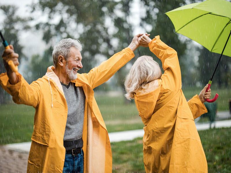 Carefree senior couple in raincoats dancing on a rainy day.