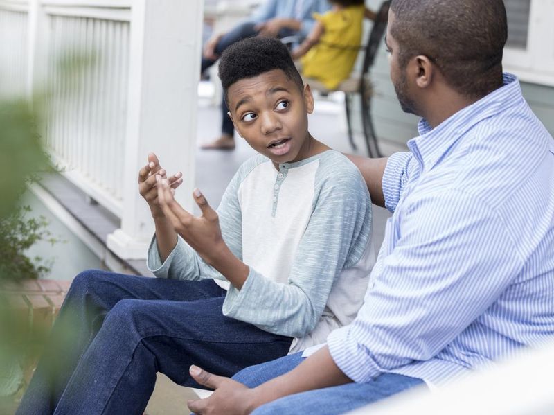 Confused preteen son talks to father on front porch
