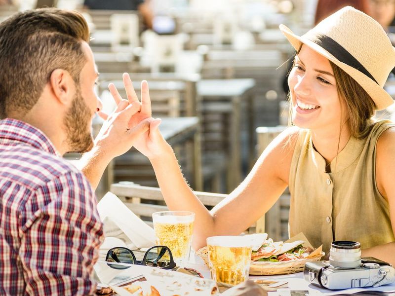 Couple in love having fun at beer bar on travel excursion - Young happy tourists enjoying happy moment at street food restaurant - Relationship concept with focus on girl face on warm bright filter