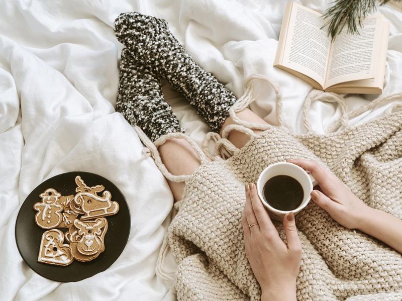 Cozy winter day at home in bed with warm knitted blanket, book, coffee and gingerbread cookies