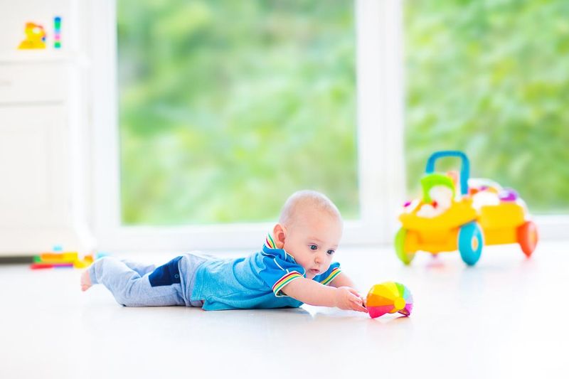 Cute baby boy playing with toy car in sunny nursery
