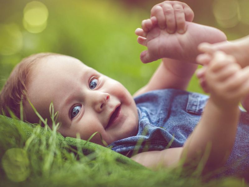 Cute baby playing with his legs on the grass