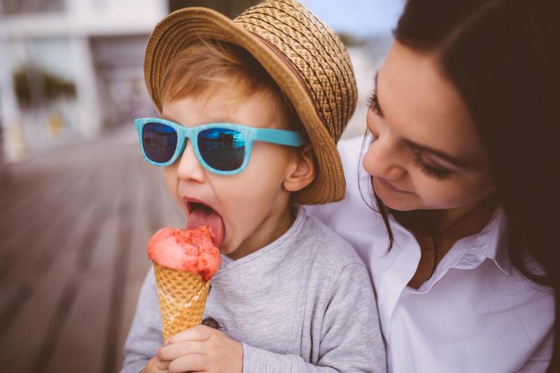 Cute young boy eating ice cream in his mother's arms