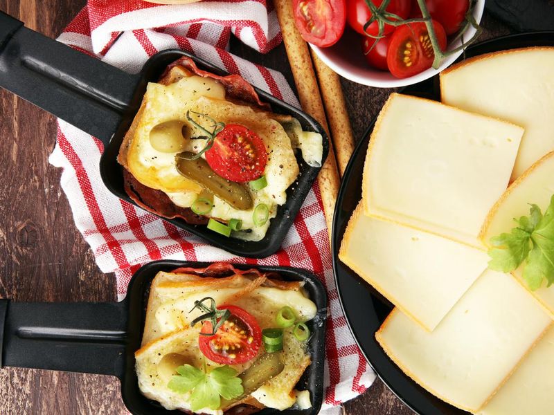 Delicious traditional Swiss melted raclette cheese on diced boiled or baked potato served in individual skillets with salami