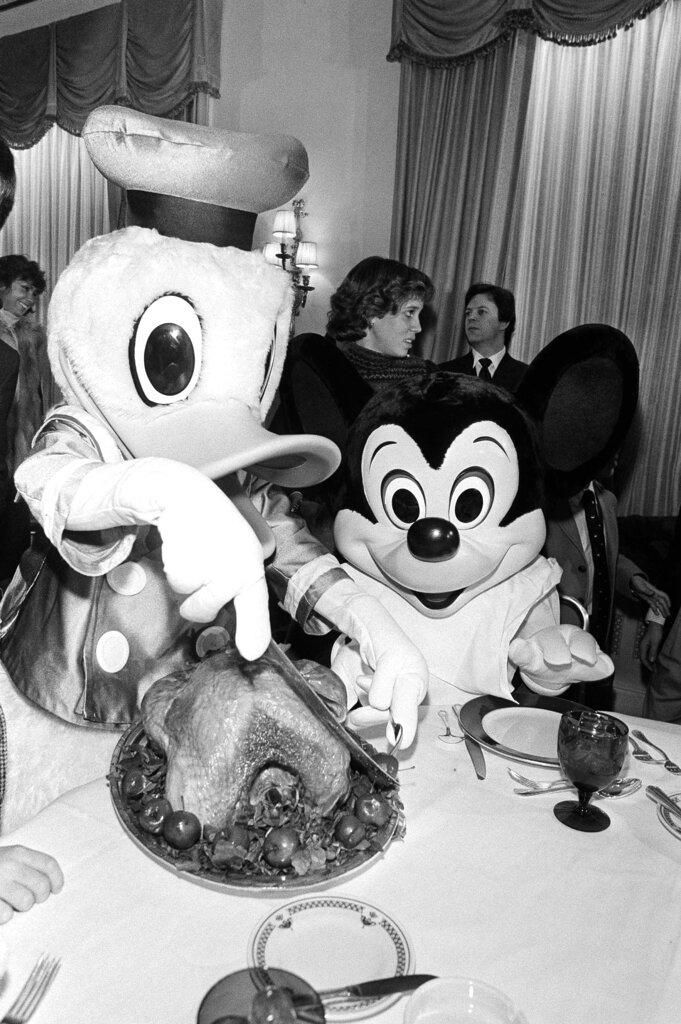 Donald Duck carves the turkey while Mickey Mouse watches