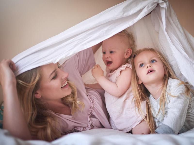 Family of three playing under a sheet on the bed at home