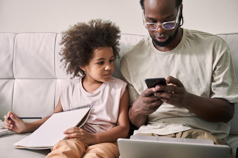 Father and his daughter using smartphone while sitting