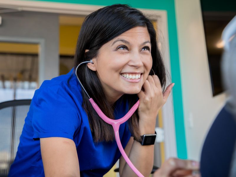Female nurse using a stethoscope while meeting with patient