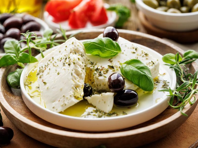 Feta cheese with the addition of olive oil, olives and herbs on a ceramic plate on a rustic wooden table