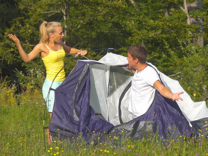 Funny shot of young couple arguing while setting up their tent on a sunny day.