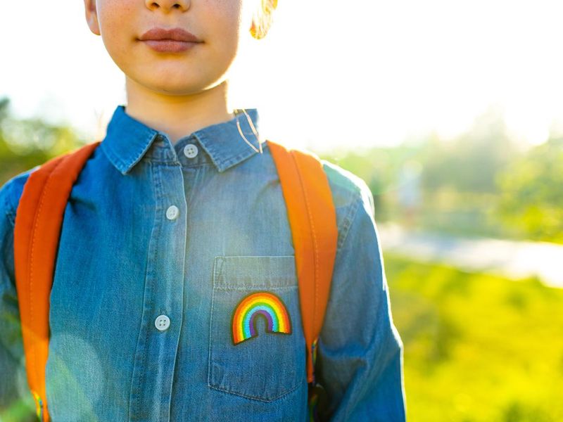 Girl in denim shirt with rainbow symbol wearing backpack