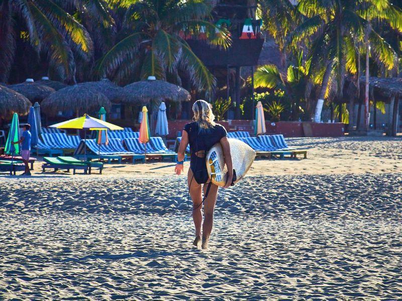 girl walking with a surf board and lounges on the background, zicatela puerto escondido oaxaca