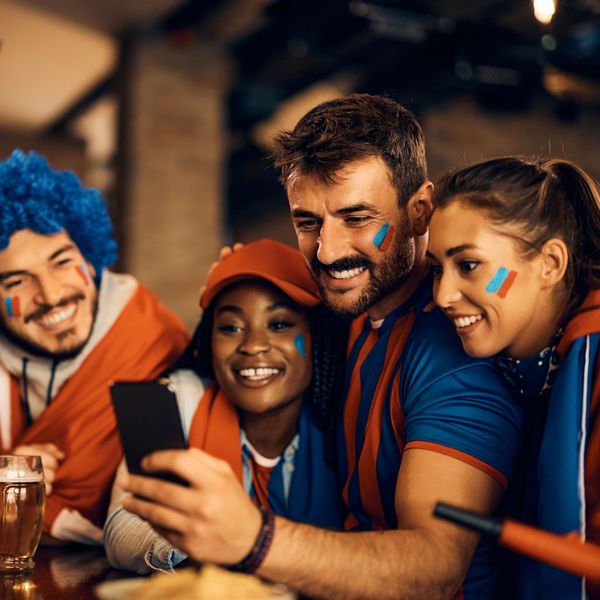 Happy soccer fan and his friends using smart phone in a pub.