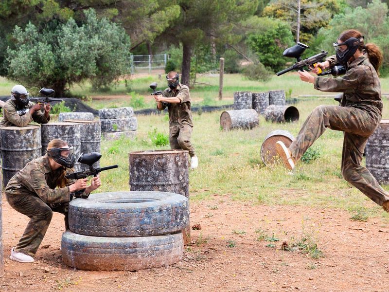 Group of people in full gear playing paintball on shooting range outdoor