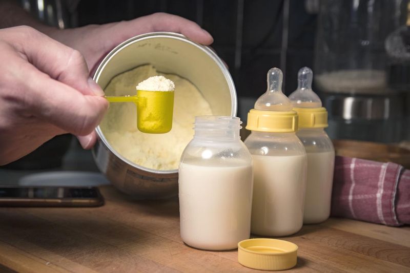 Hand holding a scoop of powdered baby formula, ready to mix in bottles