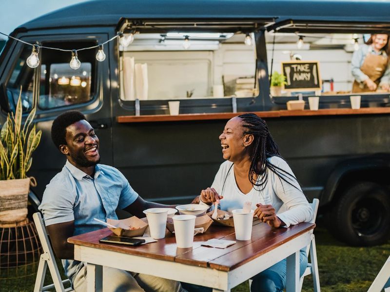 Happy black couple laughing during dinner near food truck