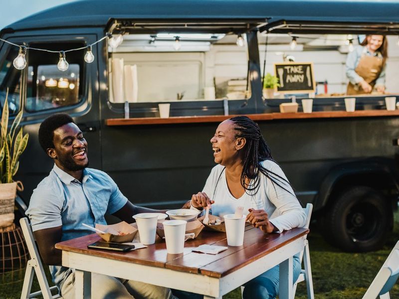 Happy black couple laughing during dinner near food truck