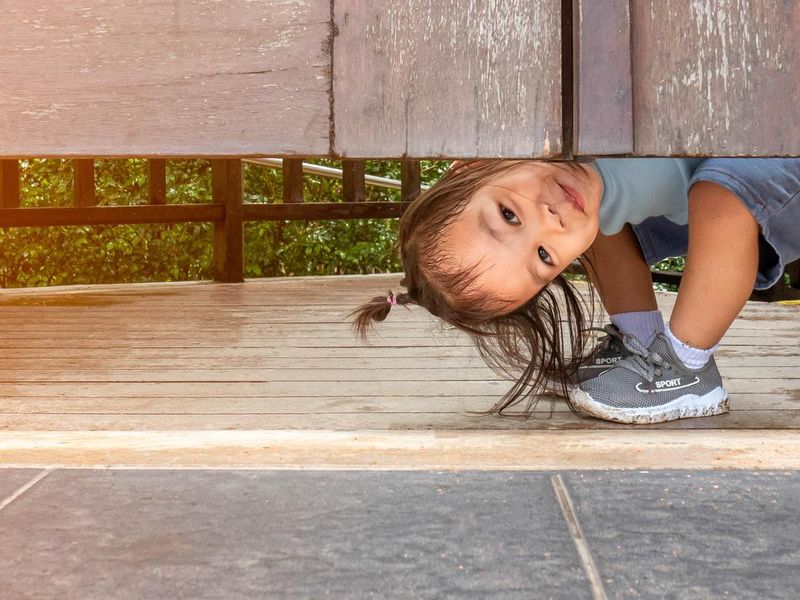 Happy kid plays peekaboo under the wooden door in the garden.