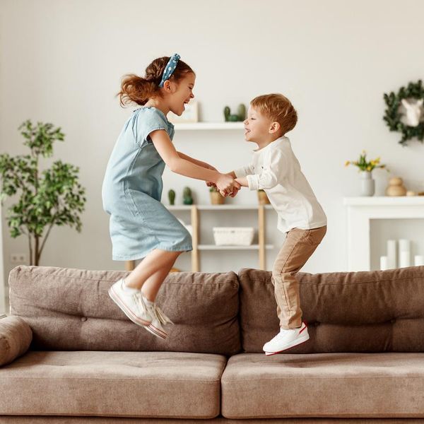 Side view of cheerful boy and girl holding hands and jumping on couch while having fun at home together