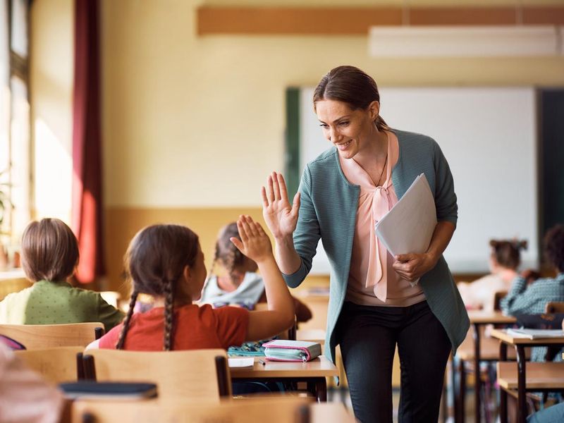 Happy teacher giving high-five to student during class