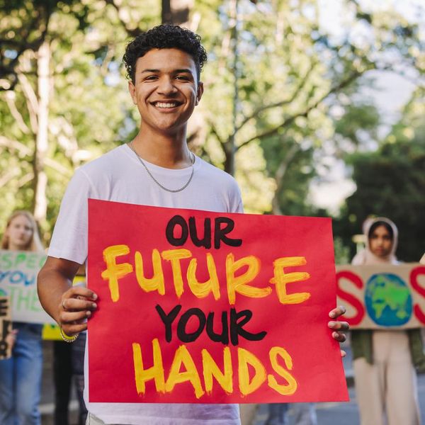 Happy teenage boy smiling at the camera while leading a march against climate change. Group of multiethnic youth activists protesting against global warming. Teenagers joining the global climate strike.