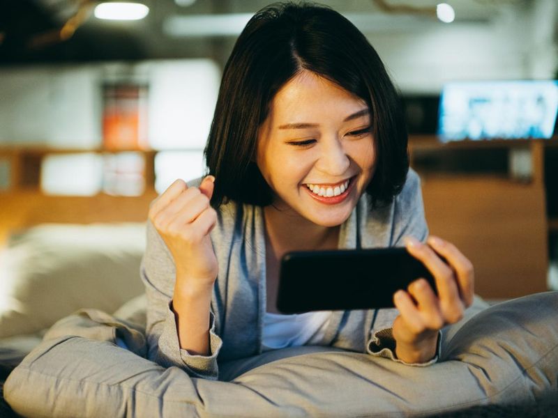Happy young woman playing mobile game on smartphone