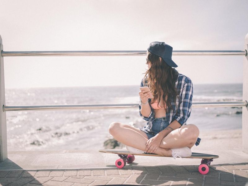 Hipster girl sitting on her skateboard at the beach