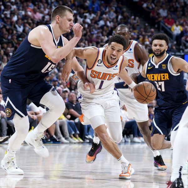 Phoenix Suns guard Devin Booker, center, drives the lane between Denver Nuggets center Nikola Jokic and guard Jamal Murray in the second half of Game 2 of an NBA second-round playoff series Monday, May 1, 2023, in Denver. (AP Photo/David Zalubowski)