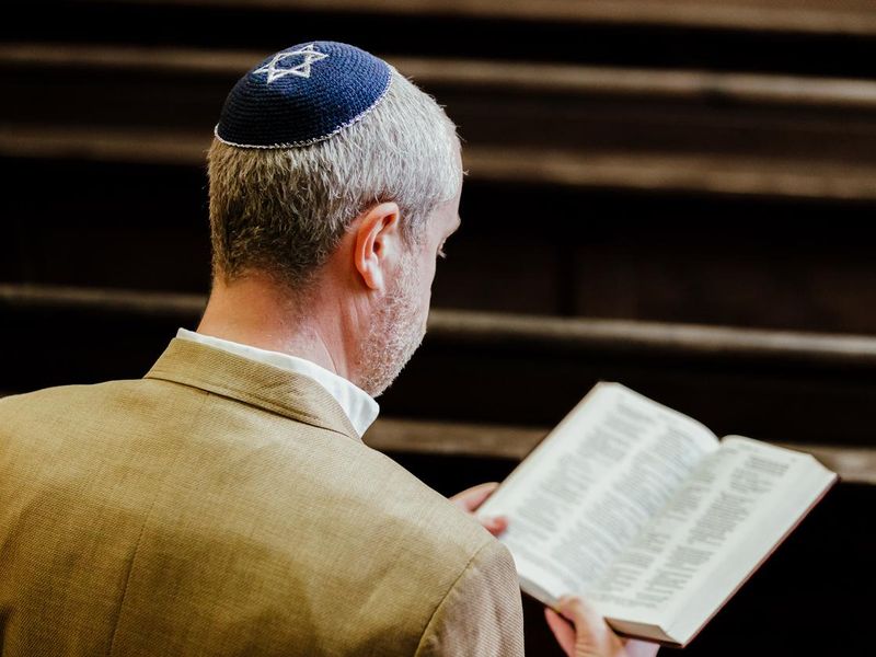 Jewish man wearing yarmulke while reading holy book in synagogue