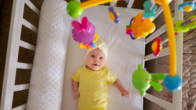 Joyful baby girl lies in white crib with mobile