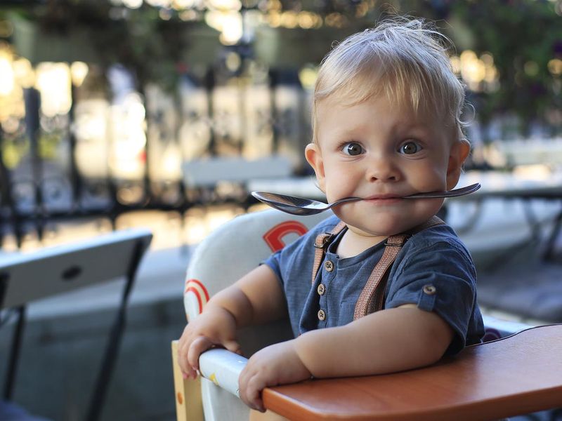 Little boy sitting in cafe with spoon in his mouth