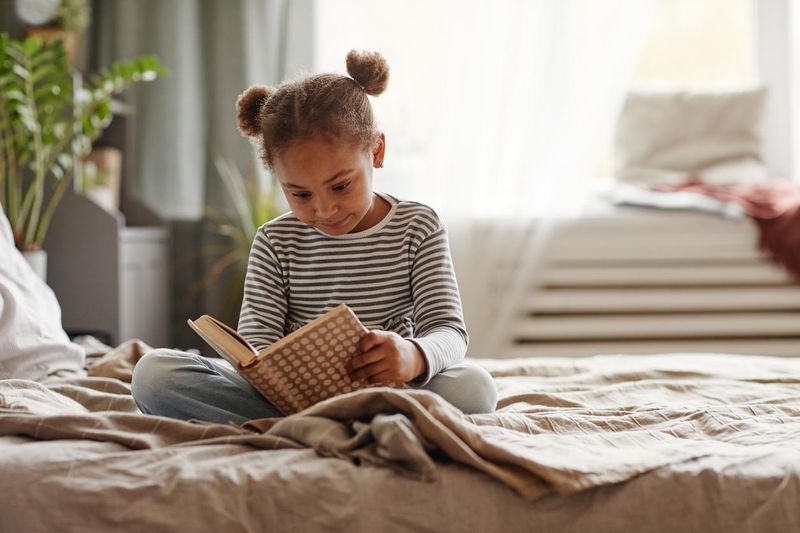 Little girl reading a book on her bed