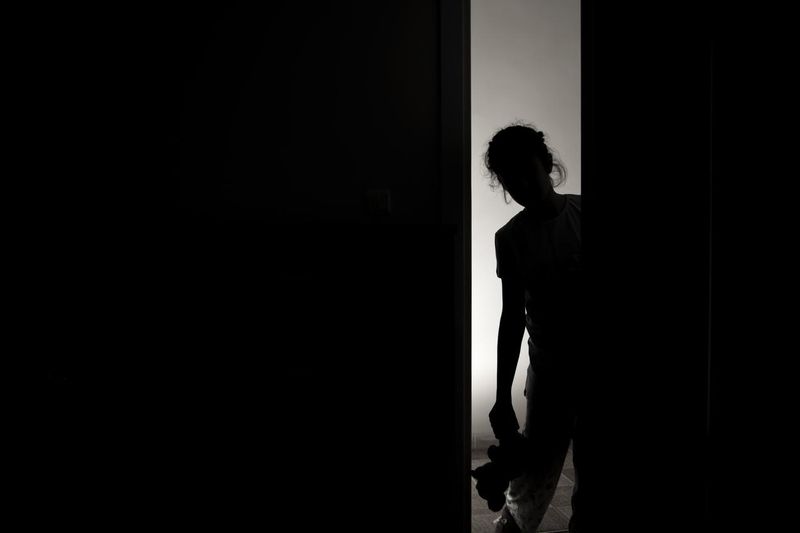 Little girl silhouette opening door into darkness