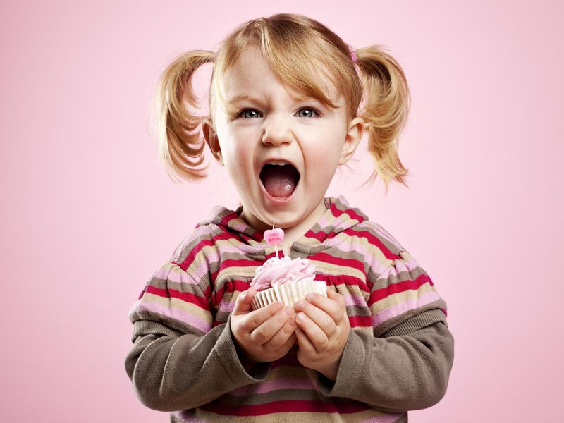 Little girl yelling and holding pink birthday cupcake
