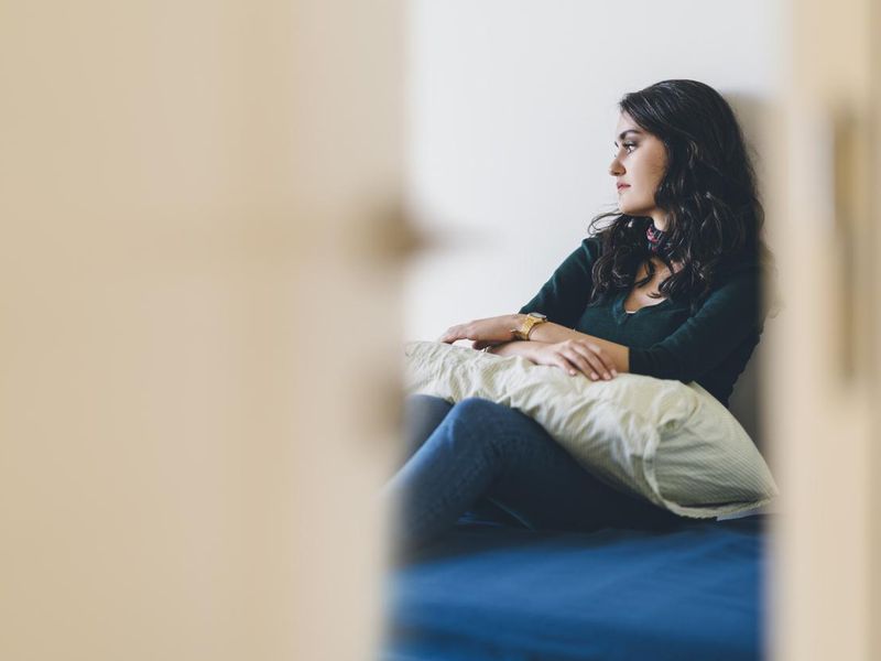 Lonely young woman sitting alone in room feeling anxious