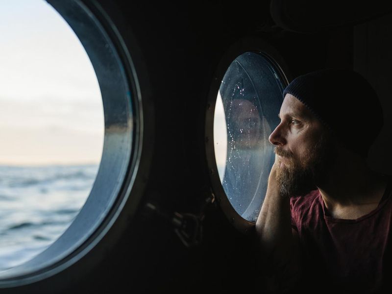 Man at the porthole window of a vessel sailing the ocean