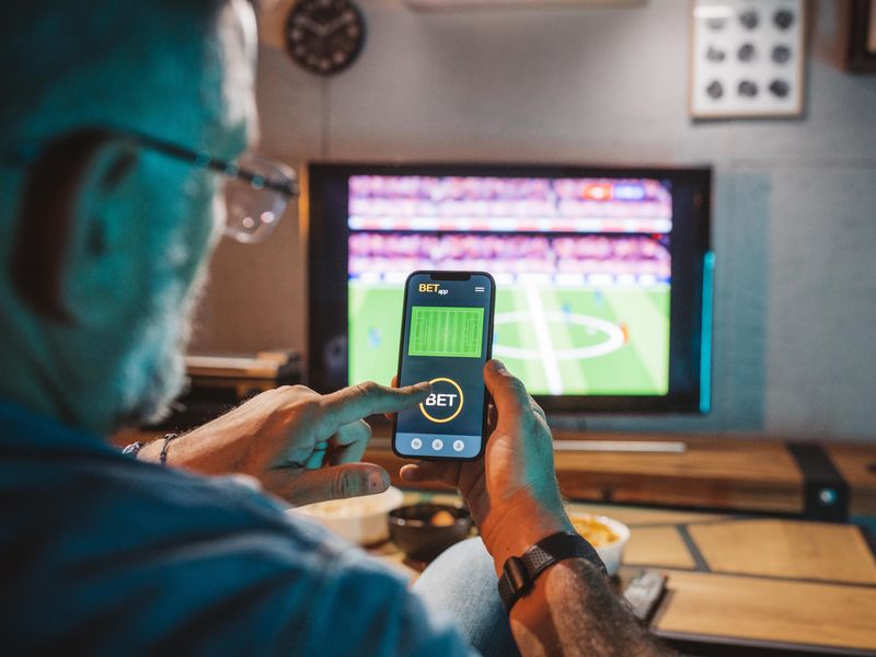 Man betting on his phone while watching soccer game at home