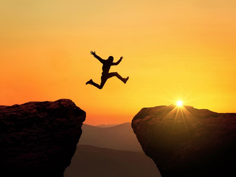 Man jumps from cliff to cliff over a precipice at sunset