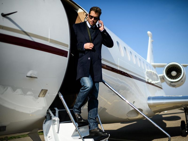 Man with sunglasses is talking over mobile phone while exiting the private jet airplane at the airport
