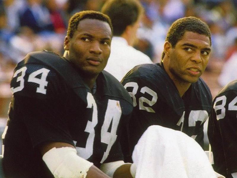 Marcus Allen and Bo Jackson sit on sidelines