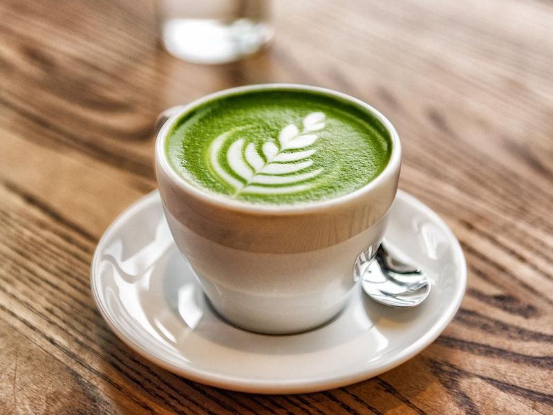 Matcha latte green milk foam cup on wood table at cafe