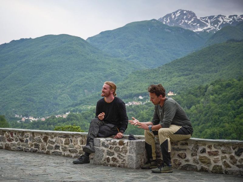Men sit on rock wall above lush valley and talk